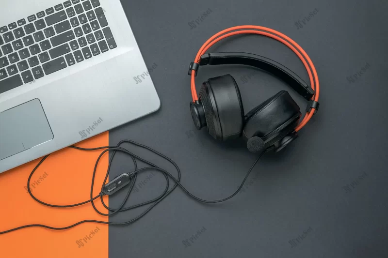 black orange headphones connected laptop black orange background creative workplace / هدفون نارنجی سیاه لپ تاپ با پس زمینه نارنجی مشکی محل کار خلاق
