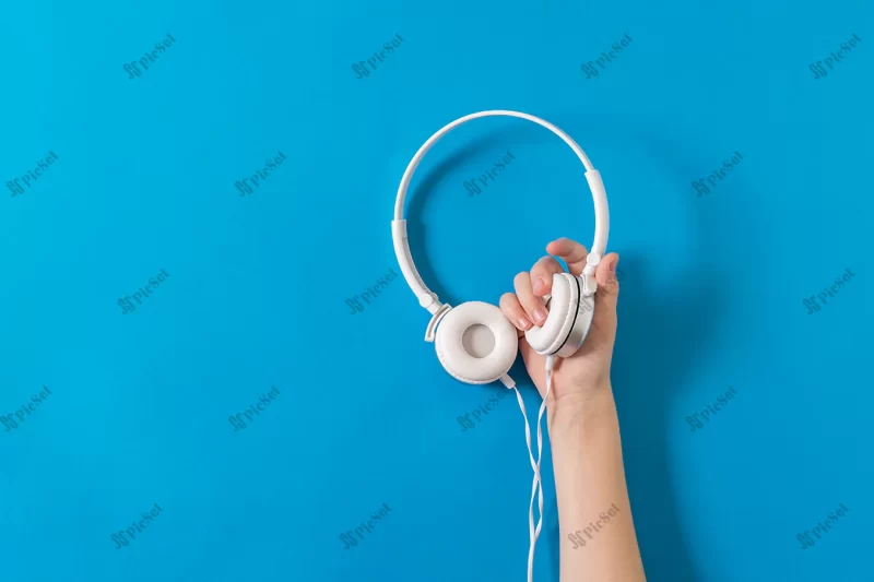 hand holding white headphones with wire bright blue background mobile audio playback equipment / پس زمینه هدفون سفید در دست