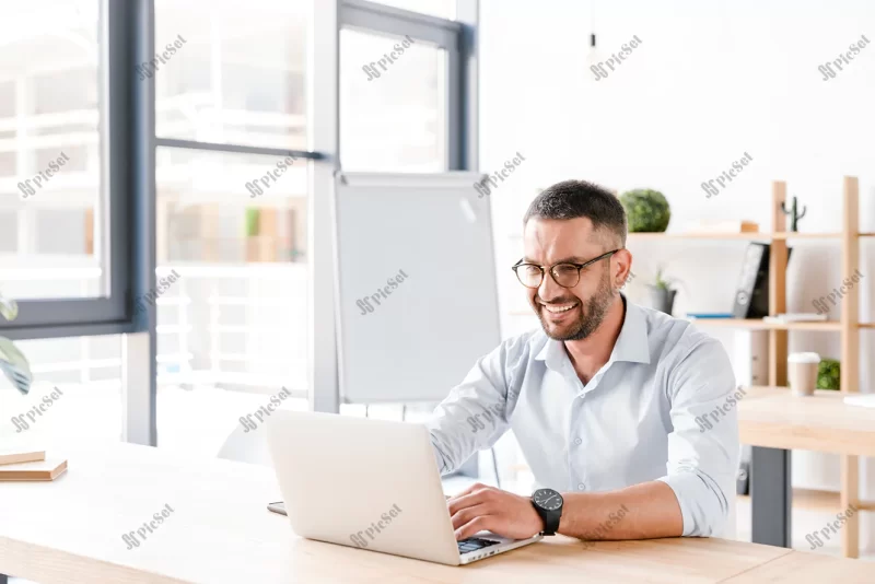 joyous office man 30s white shirt sitting desk working laptop business centre / مرد اداری شاد با پیراهن سفید روی میز نشسته با لپ تاپ کار می کند