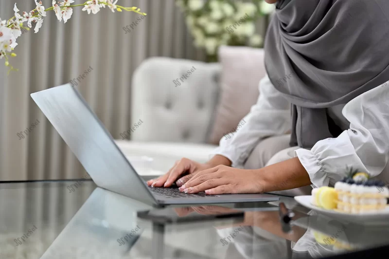 muslim woman wearing hijab living room using laptop cropped / زن مسلمان با حجاب در حال استفاده از لپ تاپ تایپ کردن و چک کردن ایمیل در خانه