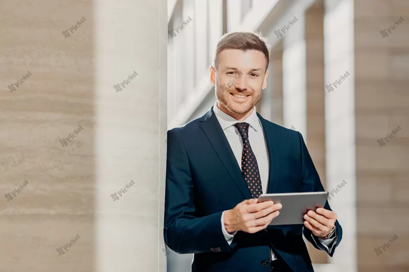 confident cheerful male lawyer reads business news has gentle smile / وکیل مرد شاد و با اعتماد به نفس با تبلت اخبار کسب و کار را می خواند